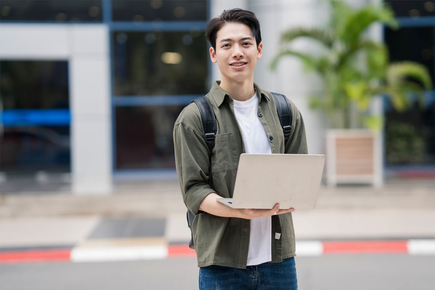 Male student outside holding laptop happy